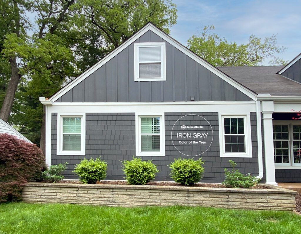 A home exterior showcasing James Hardie Iron Gray 2026 Color of the Year siding in vertical and shingle profiles, accented with crisp white trim and a natural stone retaining wall.
